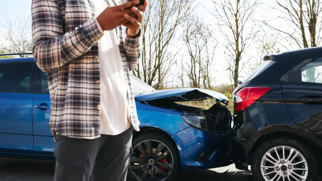 Person on the phone standing by a car with rear-end damage after an accident