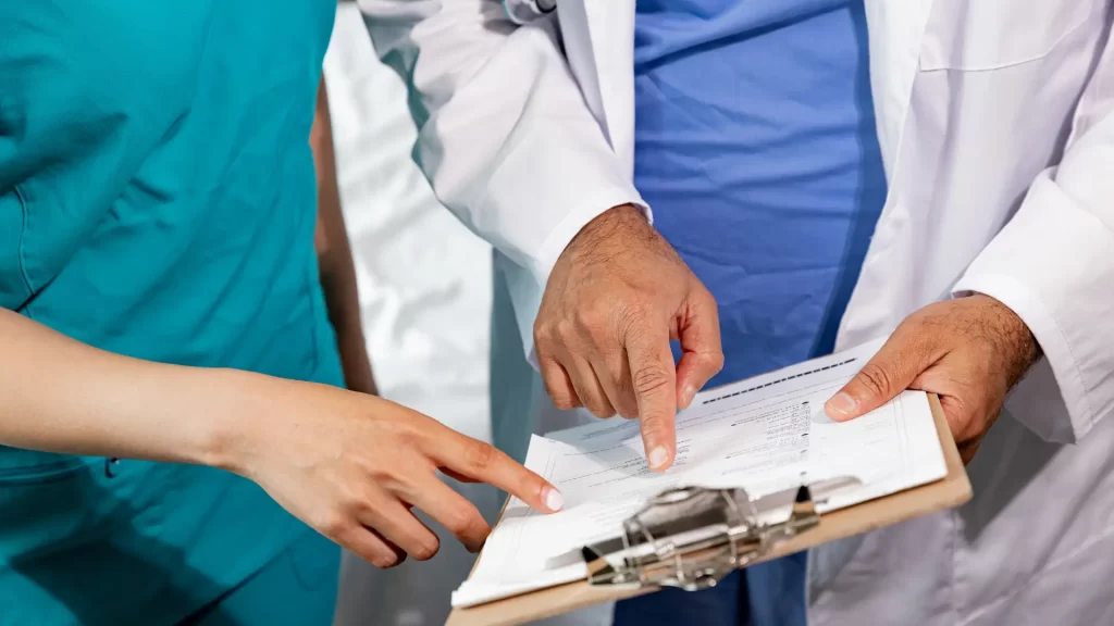 Doctor and nurse reviewing medical documents and pointing at details on a clipboard.