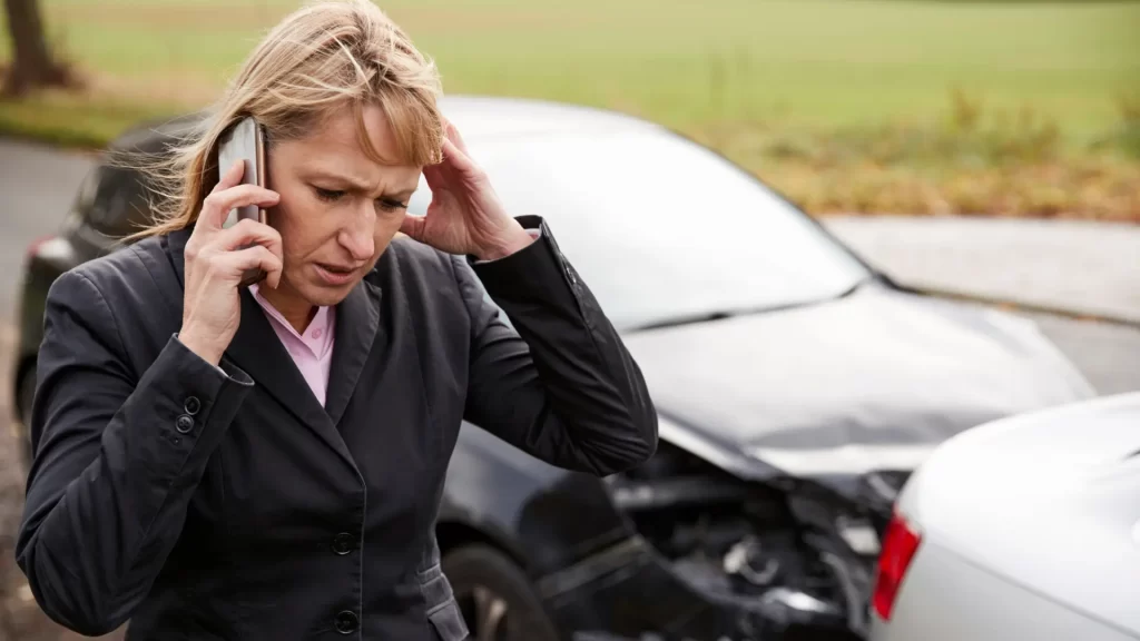 Worried woman on phone after car accident with rear damage.