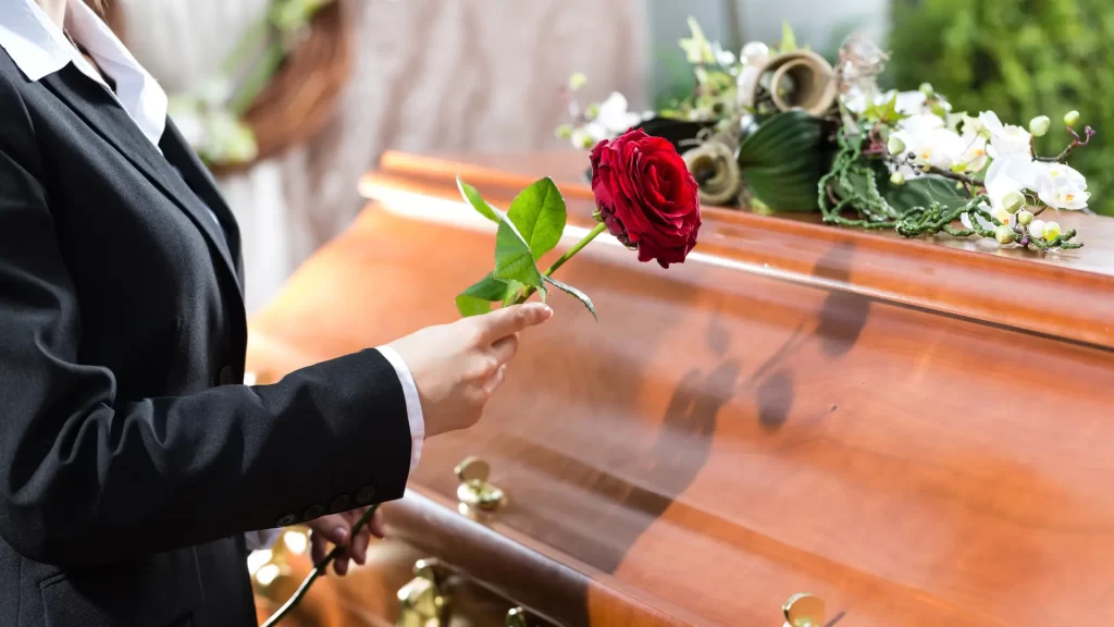 Person placing red rose on wooden casket at funeral.